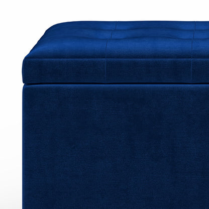 Close-up of the Cosmopolitan Upholstered Storage Ottoman—blue, rectangular, with a tufted cushioned top—set against a white background.