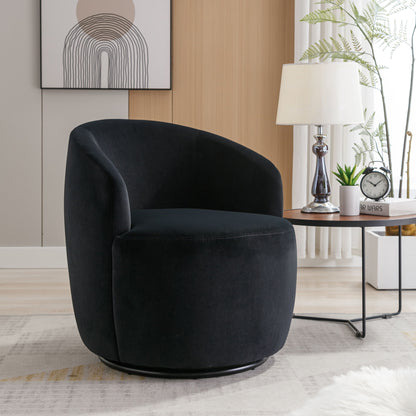 A Velvet Fabric Swivel Accent Armchair Barrel Chair with a powder-coated metal ring sits in a bright living room beside a side table holding a lamp, plant, and alarm clock; abstract art decorates the wall behind.