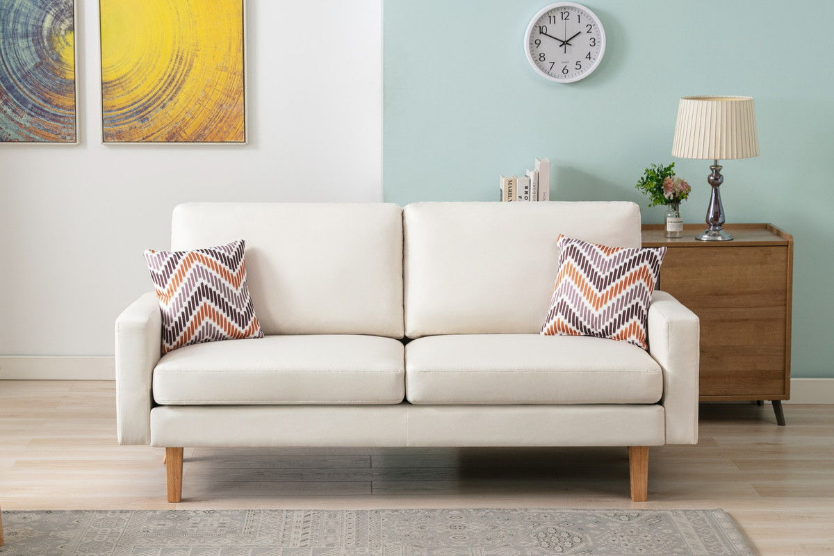 A modern living room showcases the Bahamas Sofa Set with 2 throw pillows in cream, paired with a wooden side table, lamp, decor, a wall clock, abstract artwork, and a light blue accent wall.