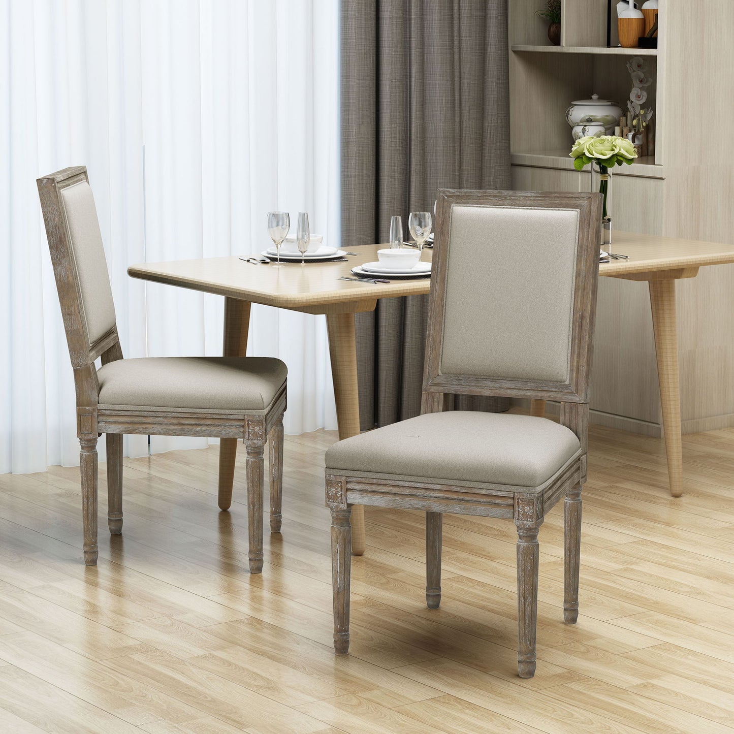 Two Traditional Style Dining Chairs With Fabric Upholstery stand near a wooden dining table set with plates, glasses, and cutlery in a modern dining room featuring light wood floors and neutral decor.