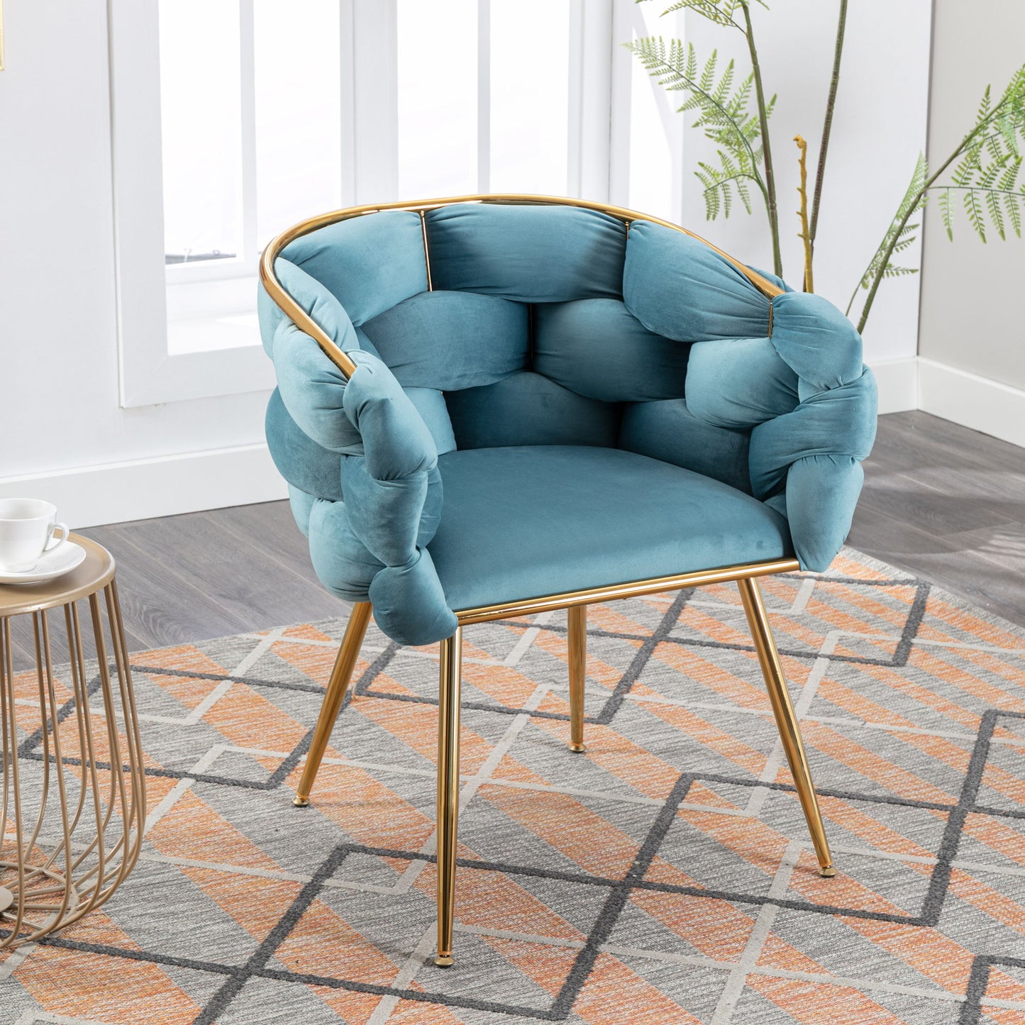 The Luxury Modern Simple Leisure Velvet Single Sofa Chair, featuring plush blue upholstery and gold metal legs, sits on a patterned rug in a bright room with light wood flooring, side table, and green plant.
