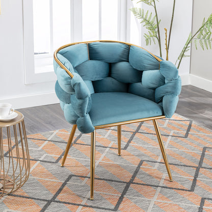 The Luxury Modern Simple Leisure Velvet Single Sofa Chair, featuring plush blue upholstery and gold metal legs, sits on a patterned rug in a bright room with light wood flooring, side table, and green plant.
