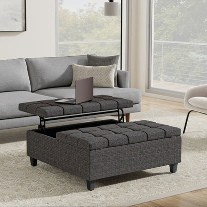 A modern living room features a gray sofa and the Harrison Upholstered Coffee Table Storage Ottoman with a lift-top for a laptop, set on a patterned rug by large windows overlooking trees and a balcony.