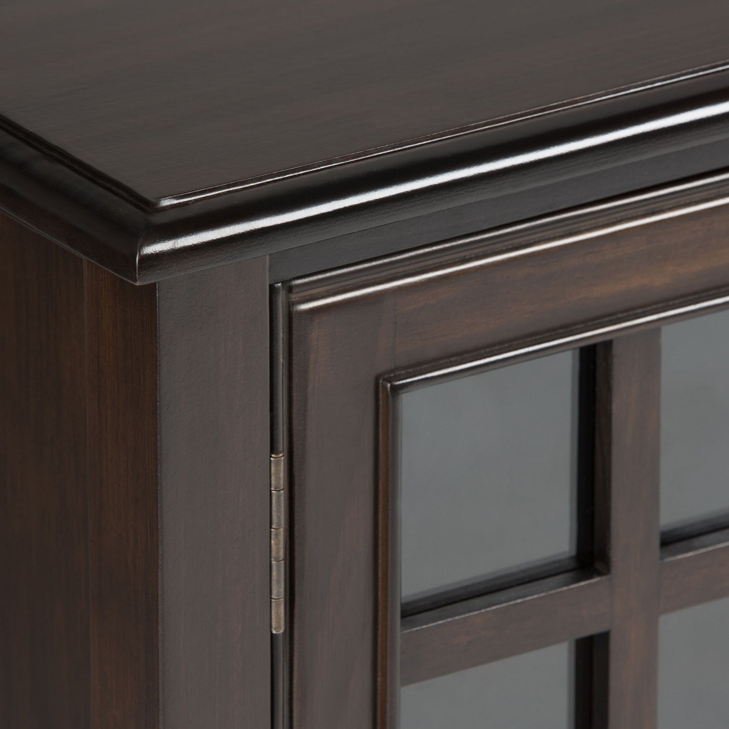 Close-up of the top corner of the Connaught - Handcrafted Low Storage Cabinet, featuring dark wood, glass-paneled doors, decorative trim, visible hinge, and a smooth finish.