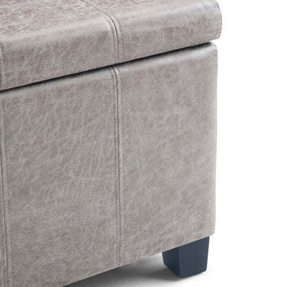 Close-up of the corner of the Dover - Upholstered Storage Ottoman Bench featuring gray faux leather, visible stitching, and dark wooden legs.
