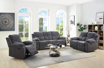 A modern living room with large windows, the Kalen Chenille 3 Piece Recliner Living Room Set in gray, a round glass coffee table, a floor lamp, decorative artwork, shelving, and light wood flooring.