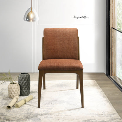 A set of Grivelle Elegant Dining Chairs in brown upholstery sits on a patterned rug in a bright room with wood flooring, decorative vases, a pendant light, and a large window. "Be yourself" is written on the wall.
