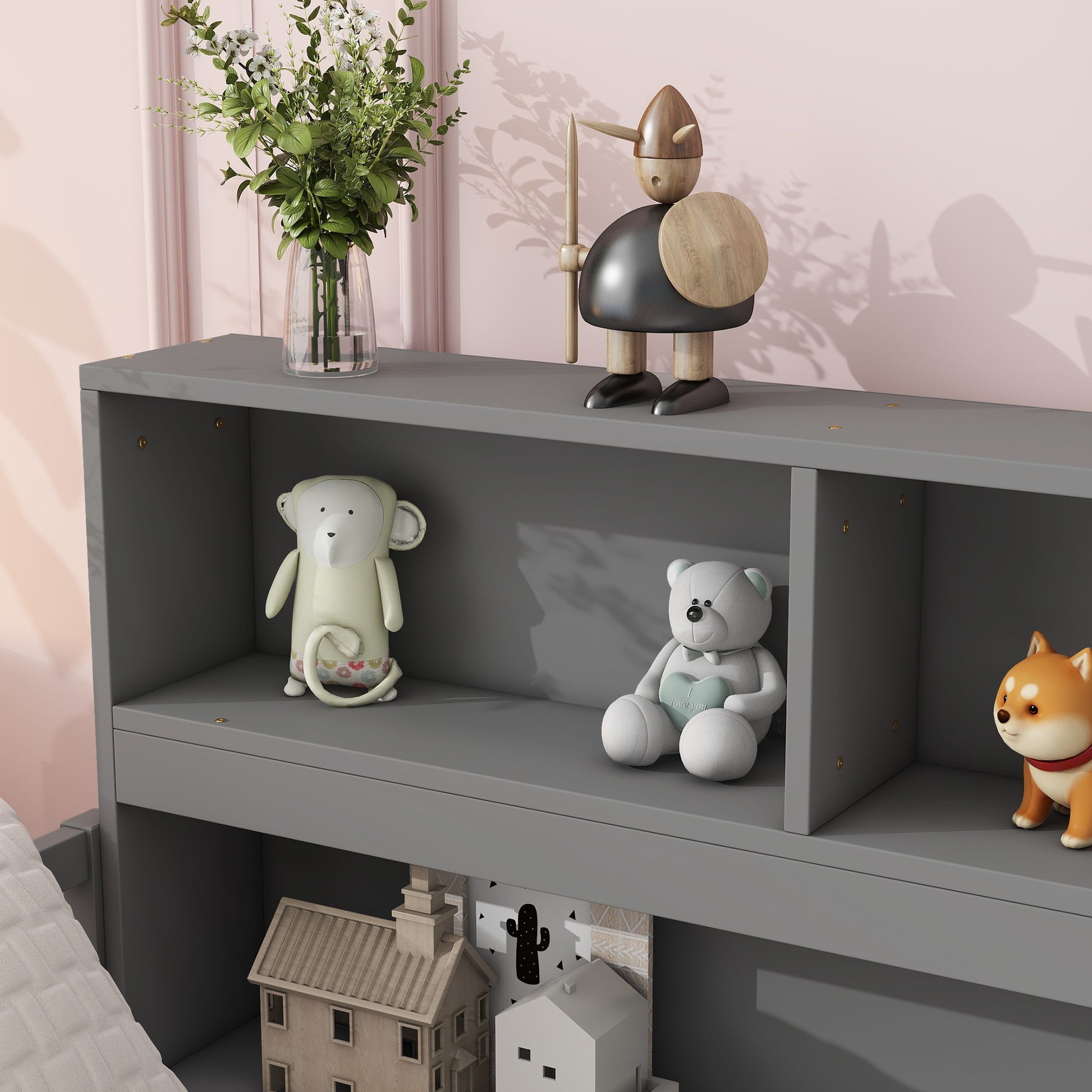A Floor Bed With Side Bookcase and shelves displays a glass vase of flowers, wooden knight figure, mouse plush, white teddy bear, toy dog, and model houses against a pink wall.
