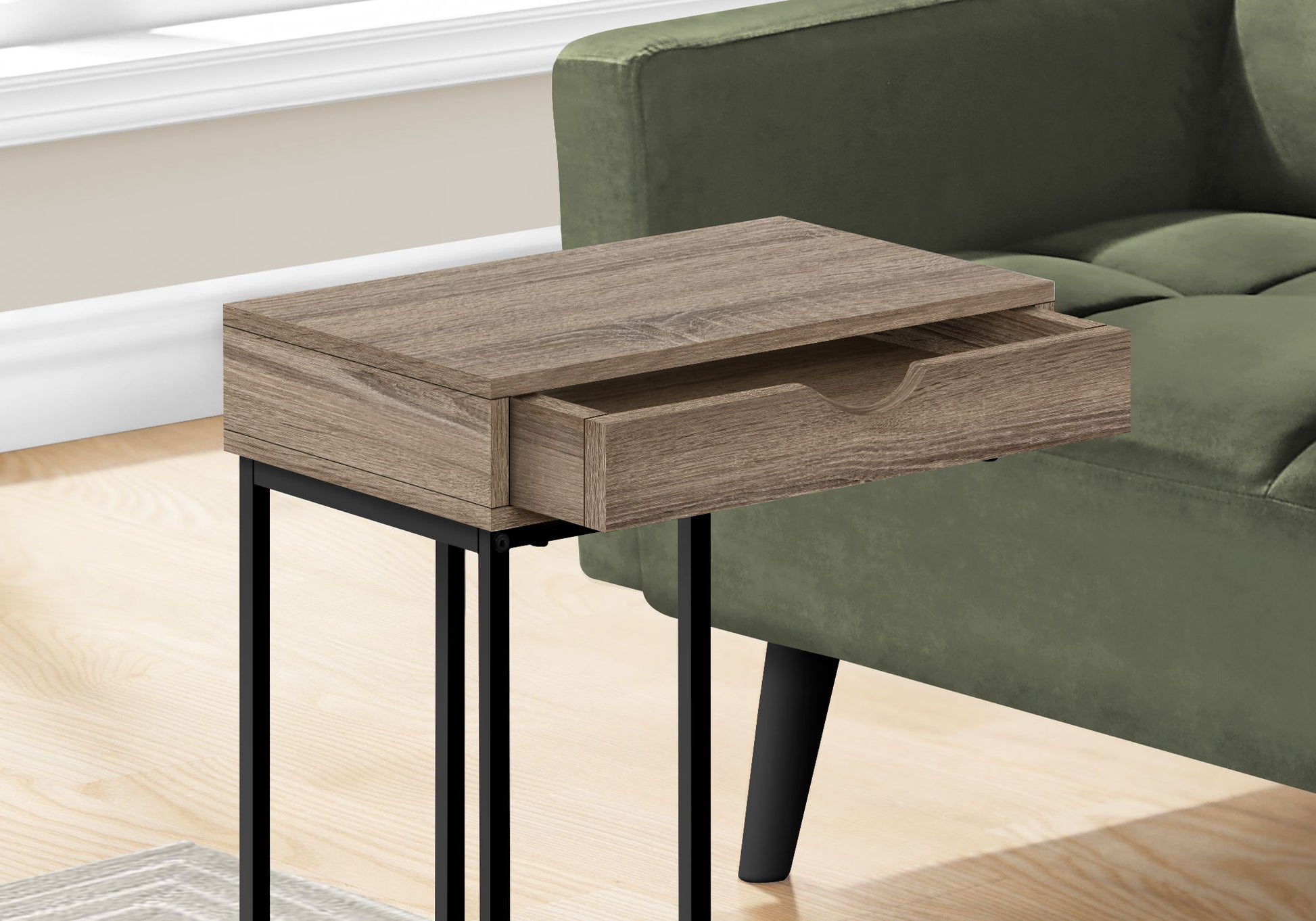 A C-shaped contemporary accent table with black metal legs stands next to a green upholstered sofa on a light wood floor, featuring a modern and versatile design.