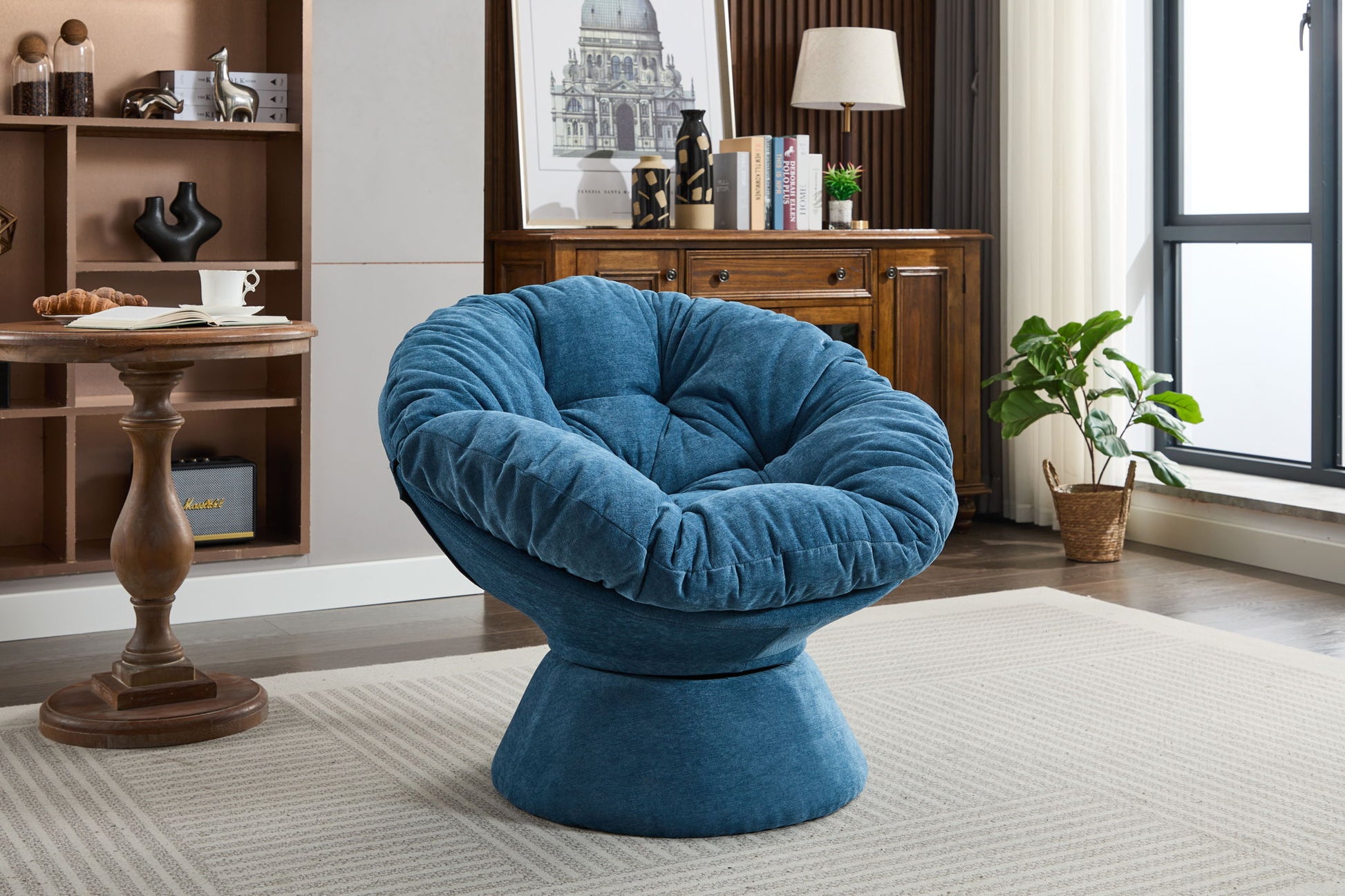 An Oversized Swivel Accent Chair in deep blue sits on a beige rug in a modern living room with wood furniture, a tall plant by the window, and shelves holding books and decor.