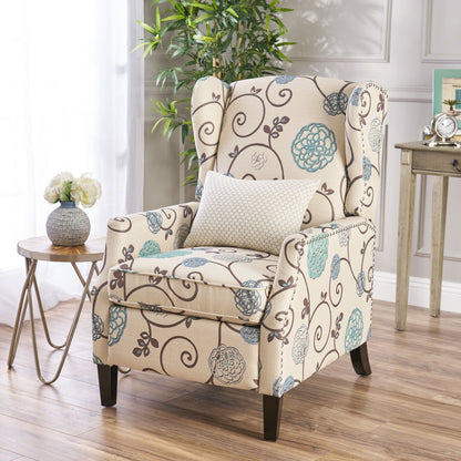 The Westeros Wing Back Fabric Upholstered Recliner, featuring beige upholstery with blue and brown florals, sits on a wooden floor with a white textured pillow. A small round table holds white flowers, and a green plant decorates the corner.