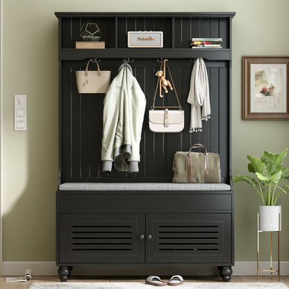 The 5 In 1 Entryway Bench features shutter-shaped doors, a cushioned seat, 4 sturdy hooks for coats and bags, and a top shelf. Nearby, there's a potted plant on the floor and a framed picture on the wall.