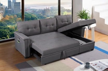 The Ashlyn Reversible Sleeper Sectional Sofa with storage chaise, USB charging ports, and pocket features tufted cushions and open chaise storage showing pillows, set in a modern living room with large windows overlooking a city park.