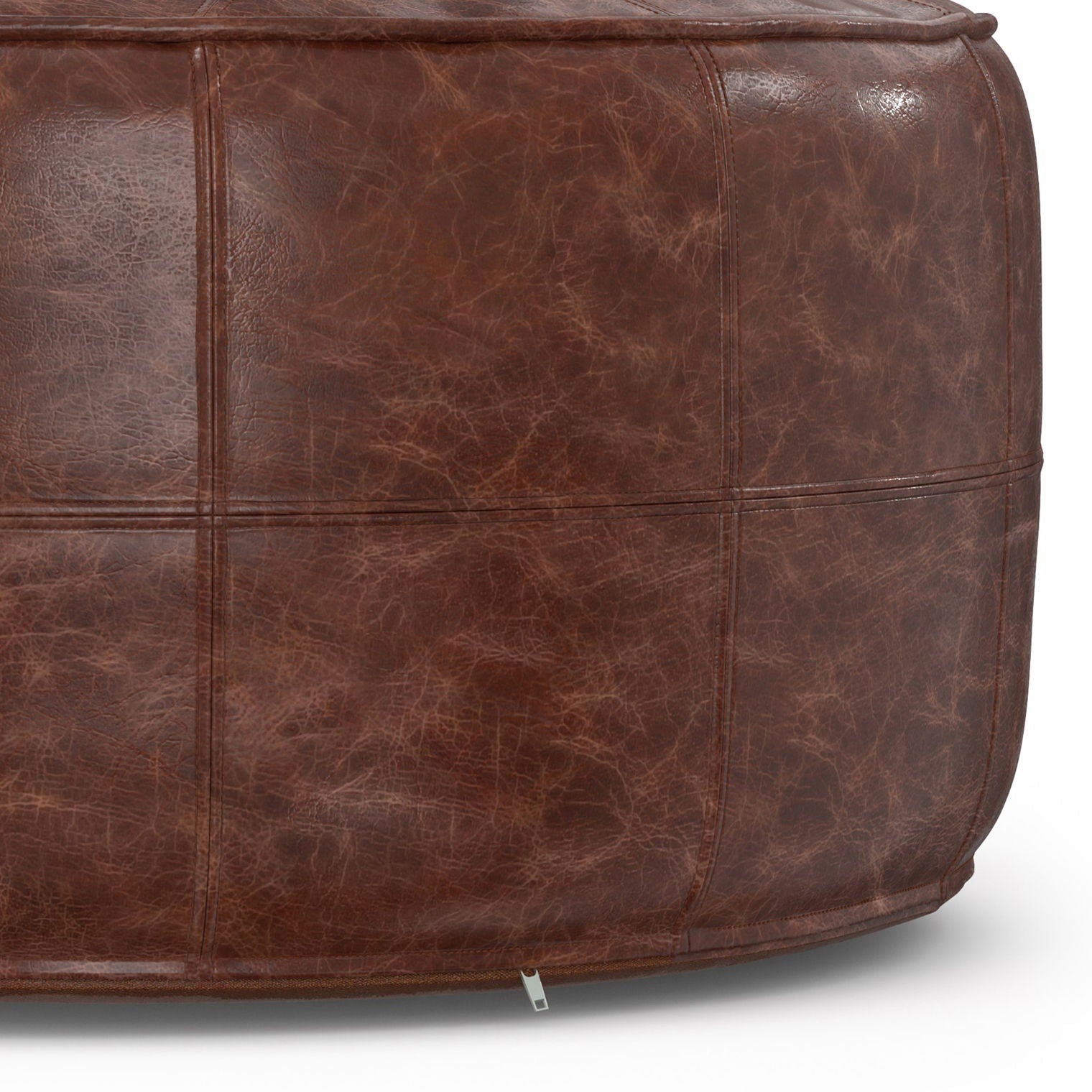 Close-up of the Connor - Handcrafted Round Pouf, featuring distressed brown leather upholstery, visible stitching, and a metal tag at the base.