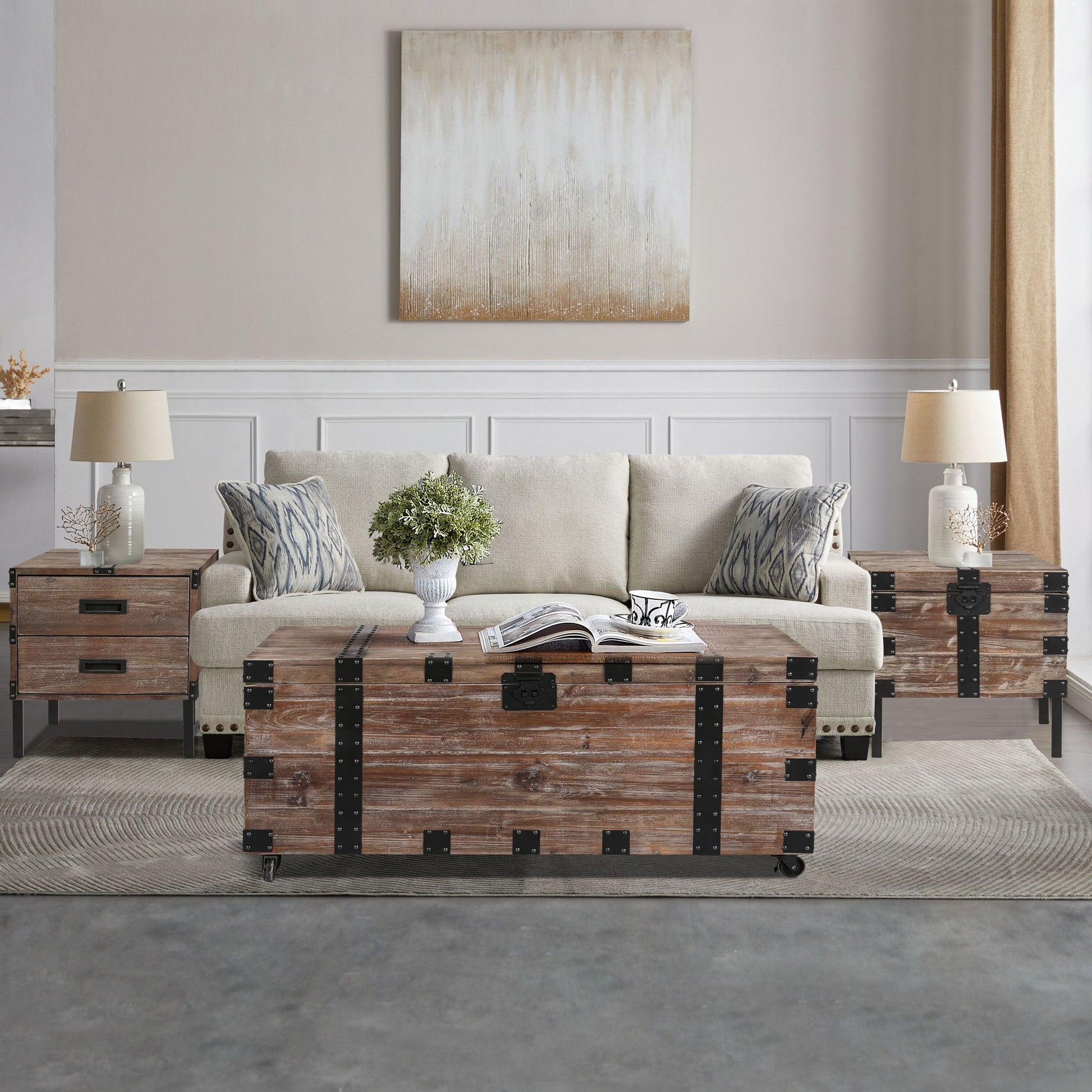 A living room with a beige sofa, two patterned cushions, the Trunk Table And Side Table With Large Storage (Set of 3) in Antique Gray, a potted plant, and a neutral abstract painting on the wall.