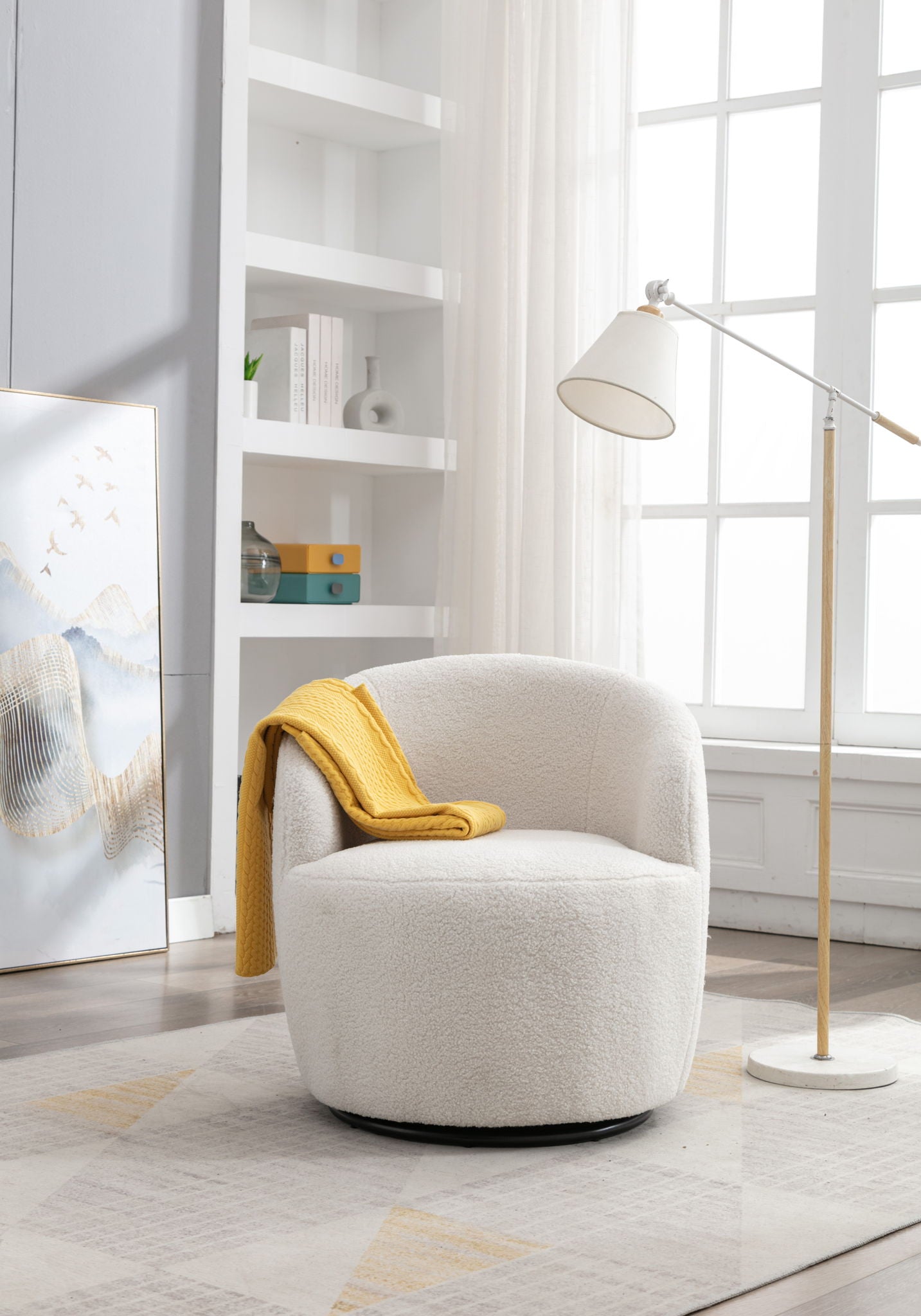 A Teddy Fabric Swivel Accent Armchair Barrel Chair with powder coating metal ring, draped with a yellow blanket, sits on a light-patterned rug near a tall window, beside a floor lamp and bookshelf in a bright, airy room.