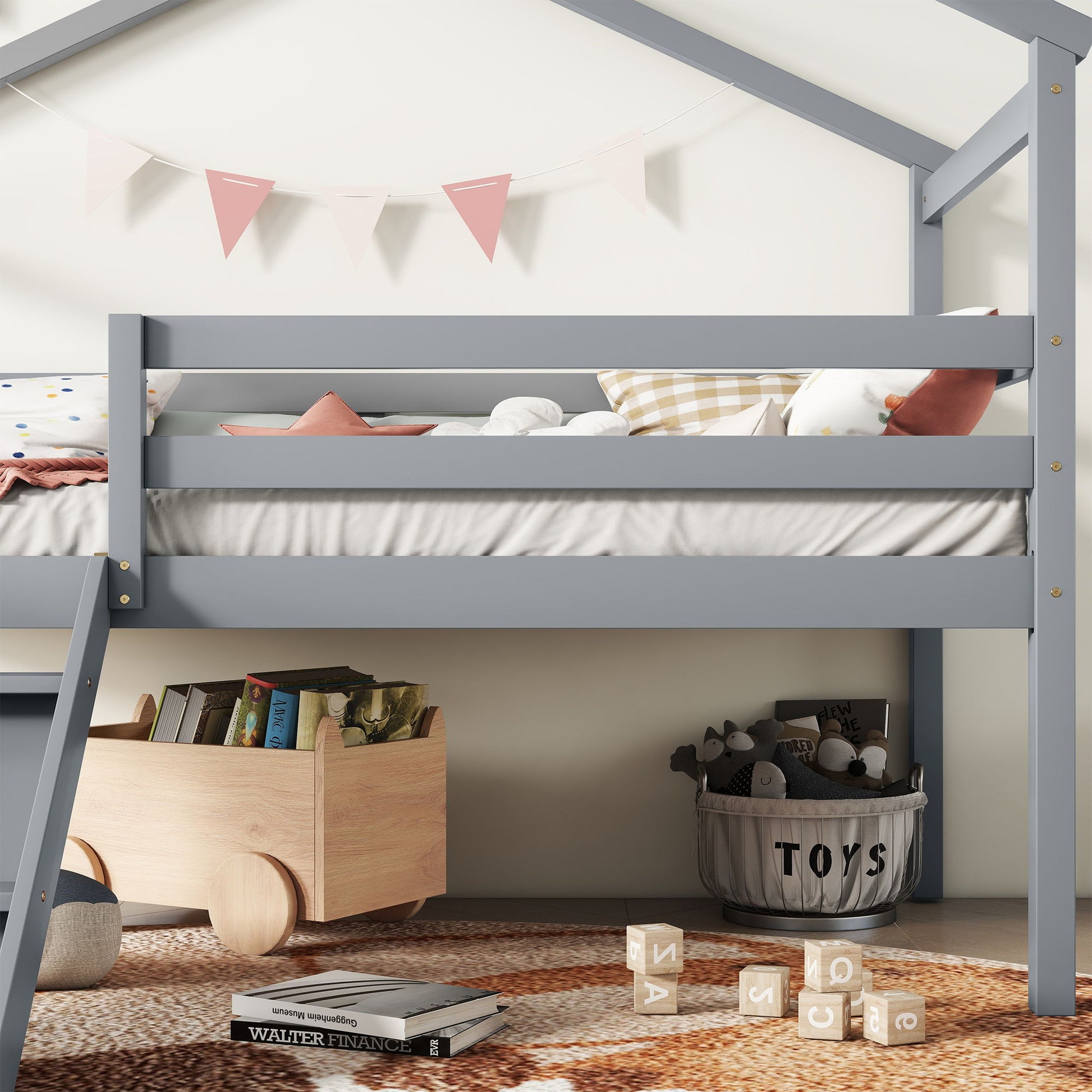 A cozy children’s room features the Low Loft House Bed With Slide, Ladder, Safety Guardrails, House Roof Frame in gray with pink and white bunting, a toy cart of books, stuffed animals in a basket, wooden blocks, and a textured rug on the floor.