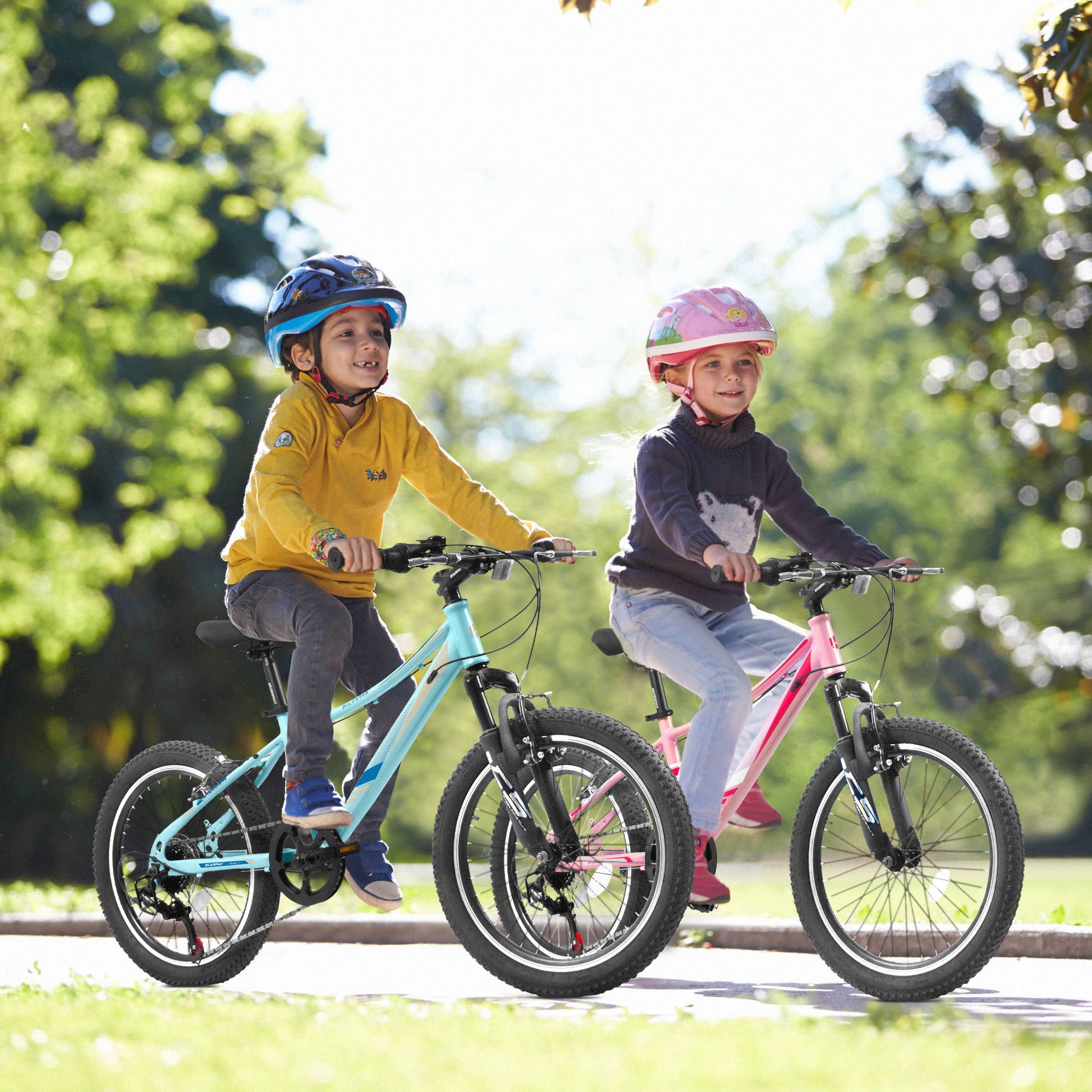 Two children wearing helmets ride S20101 20" Kids' Bikes outdoors—one on a blue, one on a pink—smiling with trees and greenery in the background. The bikes feature 7 speeds, front suspension, disc and V-brakes, and sturdy steel frames.