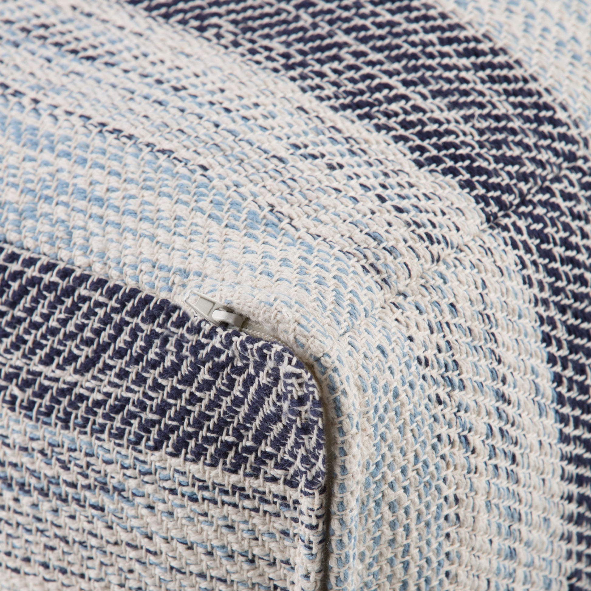 Close-up of the Clay - Square Pouf, Upholstered, featuring a woven fabric with blue, white, and light blue stripes. A small zipper is visible along the corner seam.