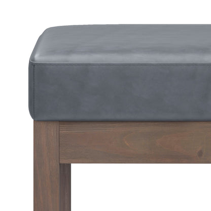Close-up of the Milltown - Upholstered Ottoman Bench, featuring a cushioned gray leather seat and wooden legs, highlighting the corner and side details against a white background.