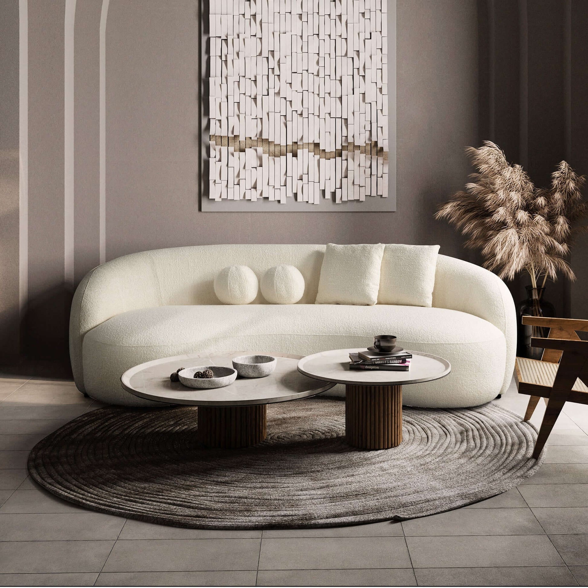 A modern living room features the Drake - Japandi Style Curvy Boucle Sofa, round white coffee tables on a circular rug, beige pampas grass in a vase, and textured wall art. The minimalist décor is finished in neutral tones.