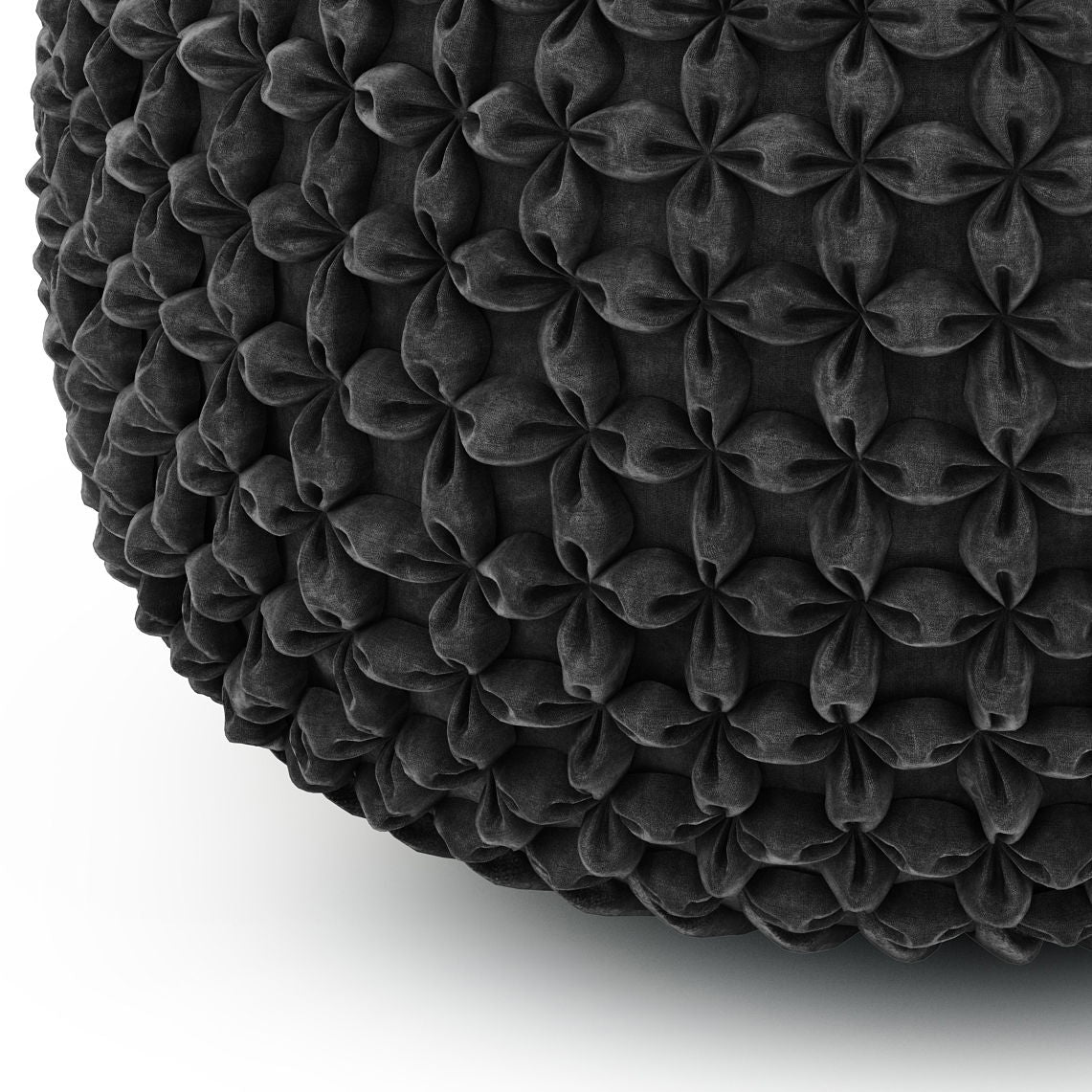 A close-up of the Renee - Handcrafted Round Pouf shows its dark, textured fabric with a repeating pattern of raised, flower-like shapes, set against a plain white background.
