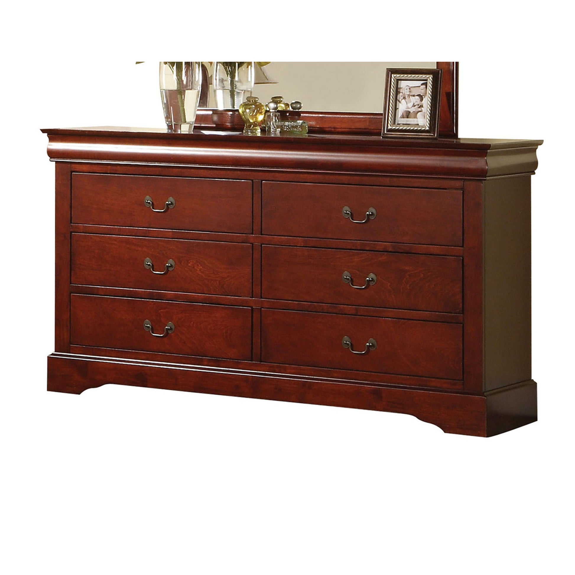 The Louis Philippe III Dresser boasts durable construction, a cherry finish, six drawers with metal handles, and elegant trim. It’s topped with a framed photo, glass vases, decorative items, and a partially visible mirror behind them.