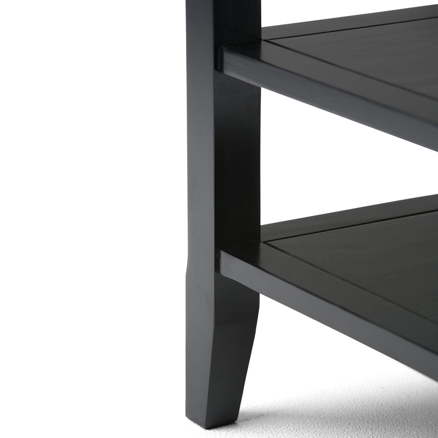Close-up of the lower corner of the Acadian - Handcrafted End Table in black wood, featuring two shelves and one leg on a light-colored surface.