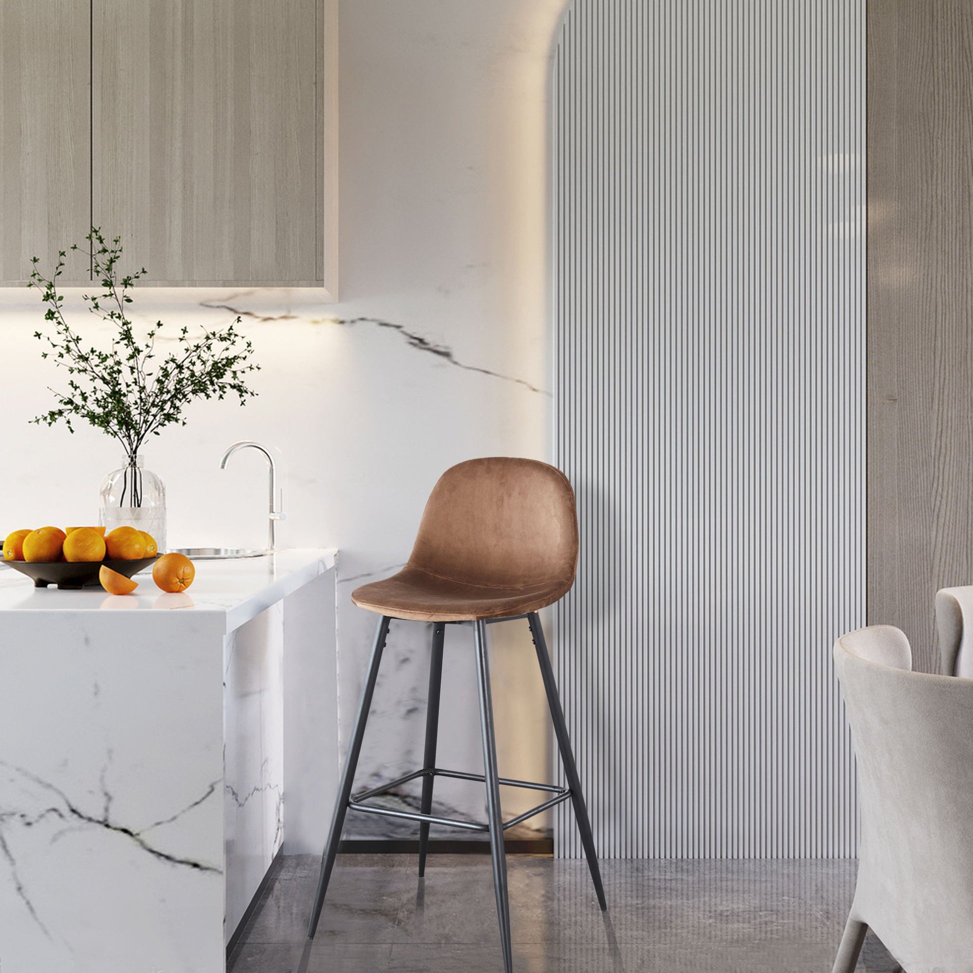 A modern kitchen features a marble countertop with oranges, a glass vase of greenery, and the Velvet Barstool With Back (Set of 2) beside the counter. Neutral cabinetry and textured wall panels complete the space.
