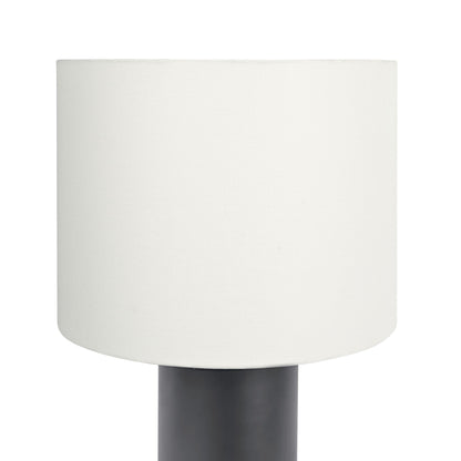 A close-up of the Aura Table Lamp featuring a cylindrical white shade and a black block base, equipped with an on/off switch, set against a plain white background.