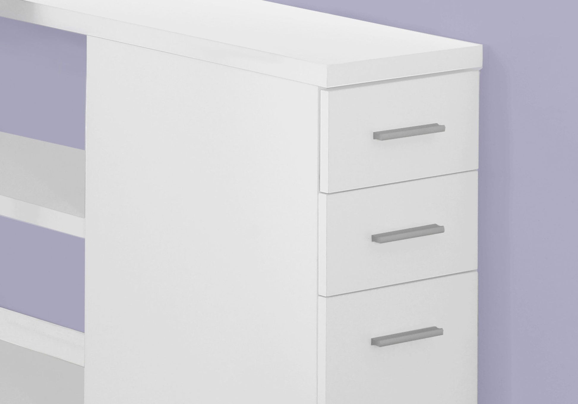 A modern white L-shaped computer desk with storage drawers and silver handles is set against a light purple wall, perfect for a contemporary home office.
