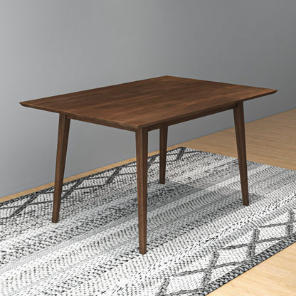 The Carlos Dining Table with angled legs stands on a patterned rug in a room featuring light wood flooring and gray walls.