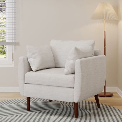 The Luminate Upholstered Fabric Club Chair with tapered legs and 2 accent pillows sits on a striped rug near a window, alongside a wooden floor lamp with a pleated shade in a softly lit room.