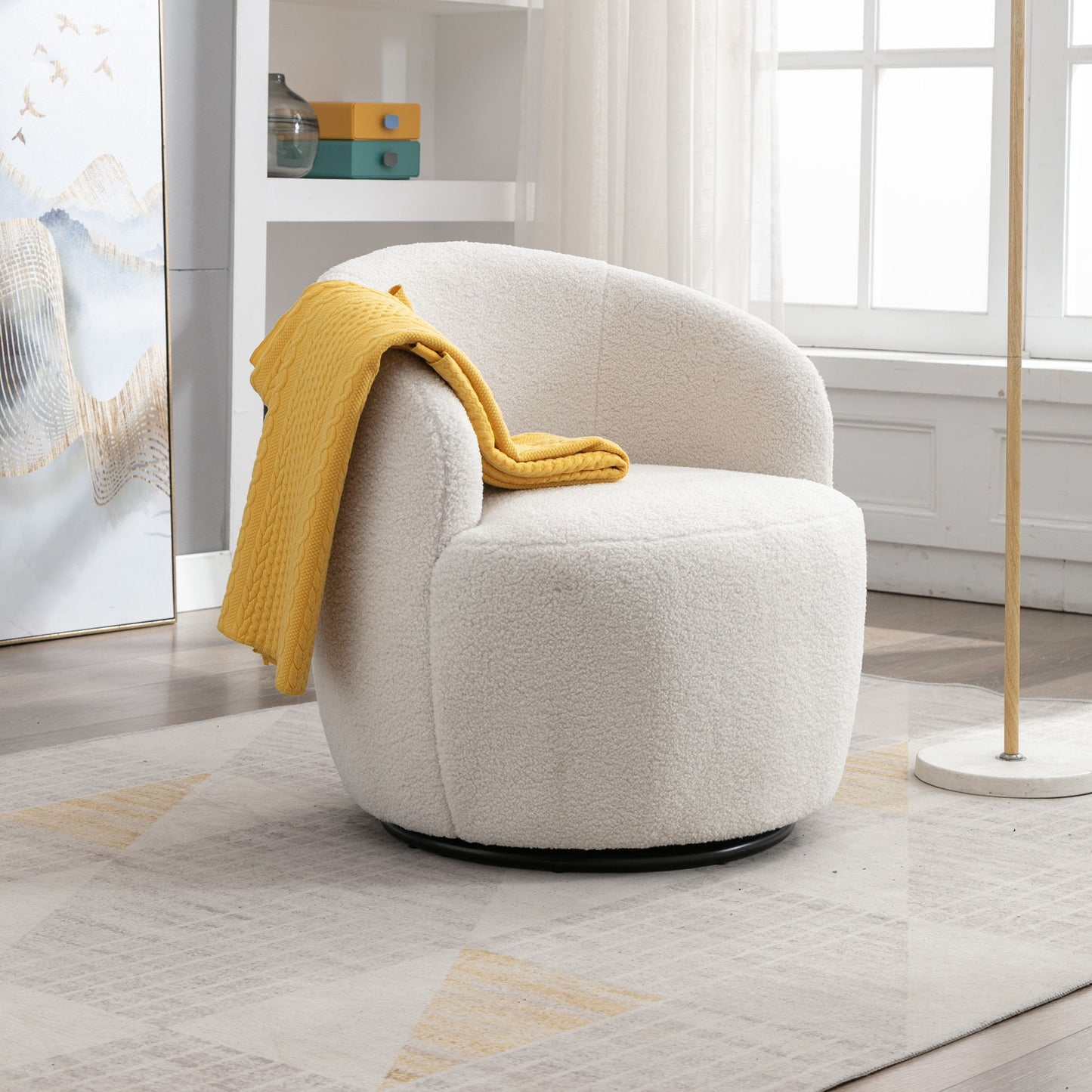 The Teddy Fabric Swivel Accent Armchair Barrel Chair with a curved backrest and powder coating metal ring sits on a geometric rug, a yellow blanket draped over the arm. Sunlight brightens the modern, minimal room through a nearby window.