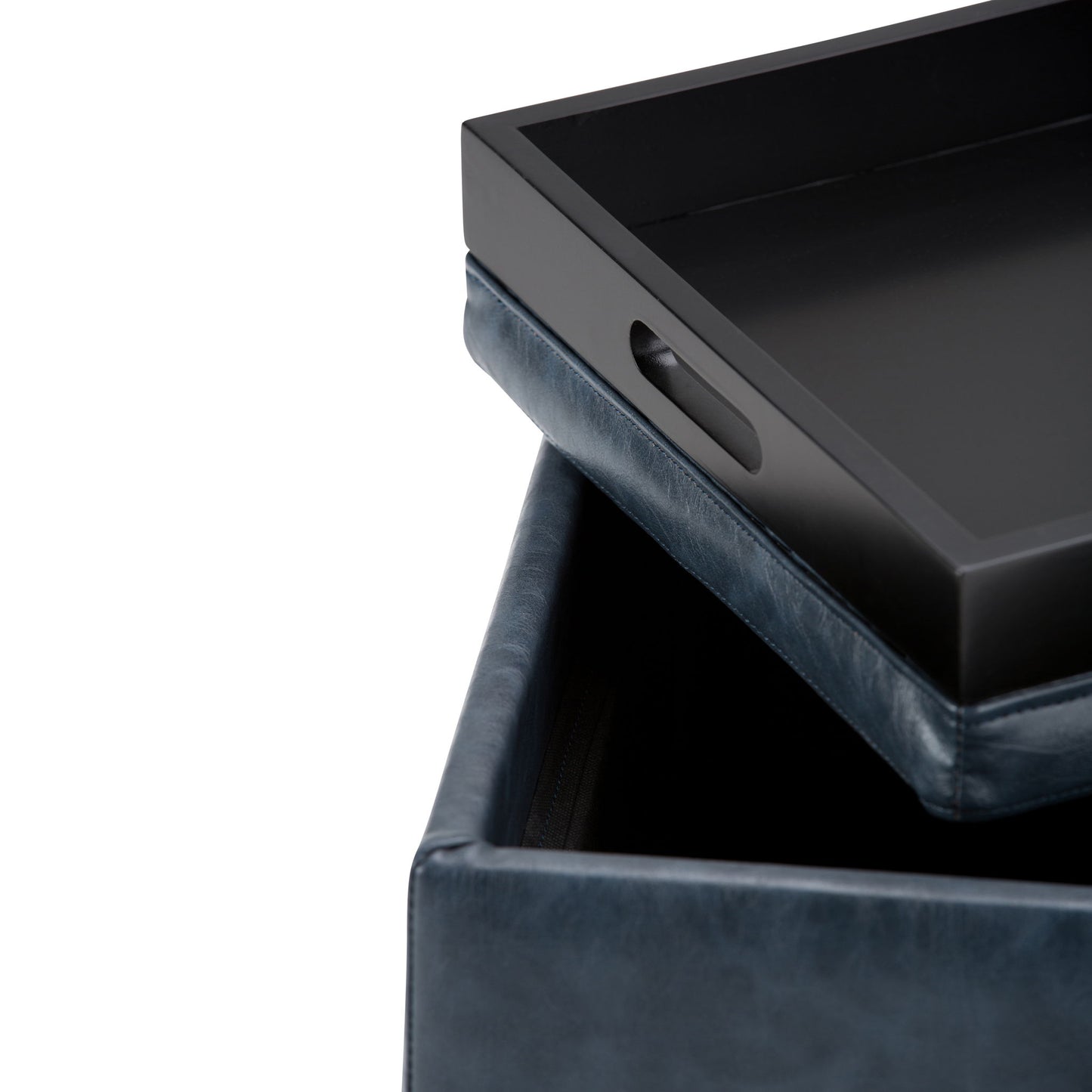 A close-up of the Rockwood Upholstered Cube Storage Ottoman With Tray in dark blue leather, showing the removable black tray with side handles partially lifted to reveal hidden storage inside.