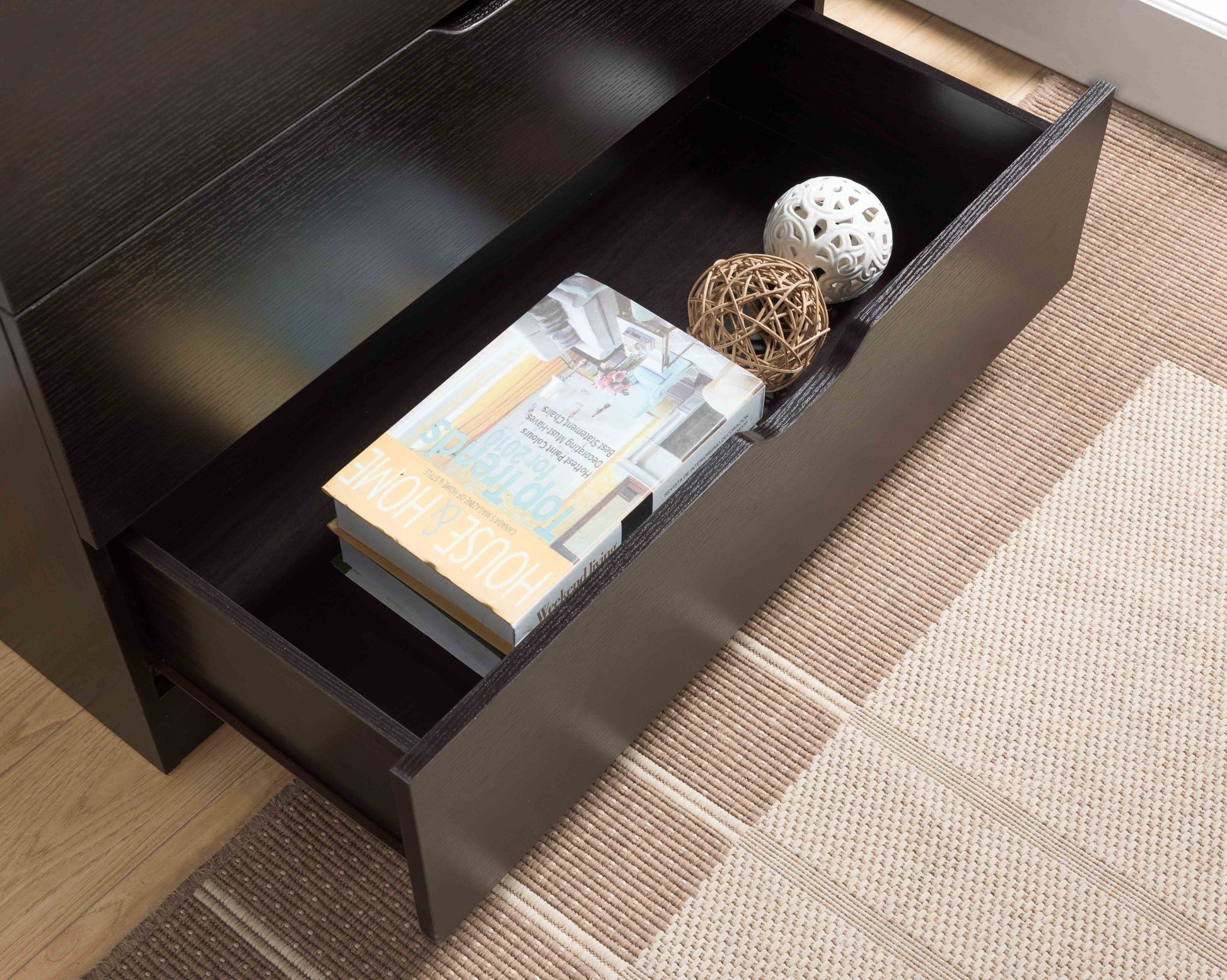 An open Modern Drawer Chest and Clothes Storage Cabinet with metal drawer glides holds a "HOUSE HOME" book, a magazine, and two decorative balls—one white, one brown—on a textured beige rug.