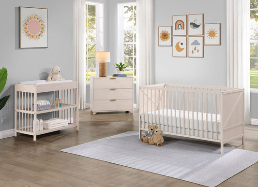 Bright nursery with the Pixie Zen 3-in-1 Crib in walnut, matching changing table and dresser. Plush toys, a lamp, and pastel art decorate the sunlit room with large windows, gray walls, and a soft rug over the wooden floor.