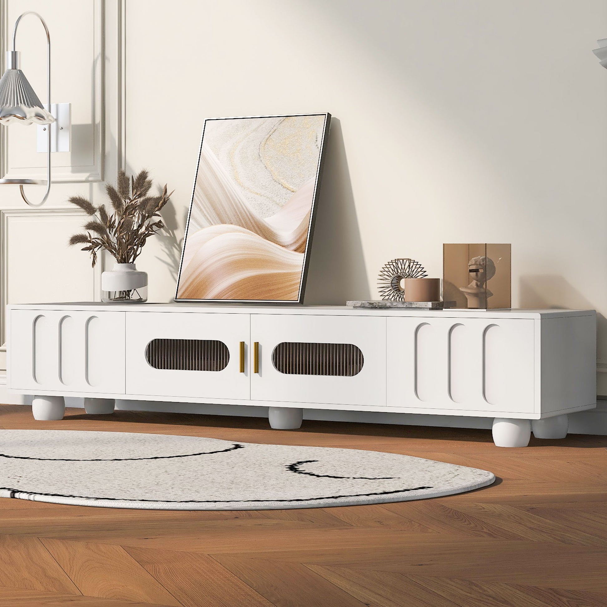 A Modern TV Stand for TVs up to 80" with glass door, 2 drawers, cabinets, solid wood legs, and metal handles displays decor and art; a round rug and hardwood floors complete the stylish living room scene.