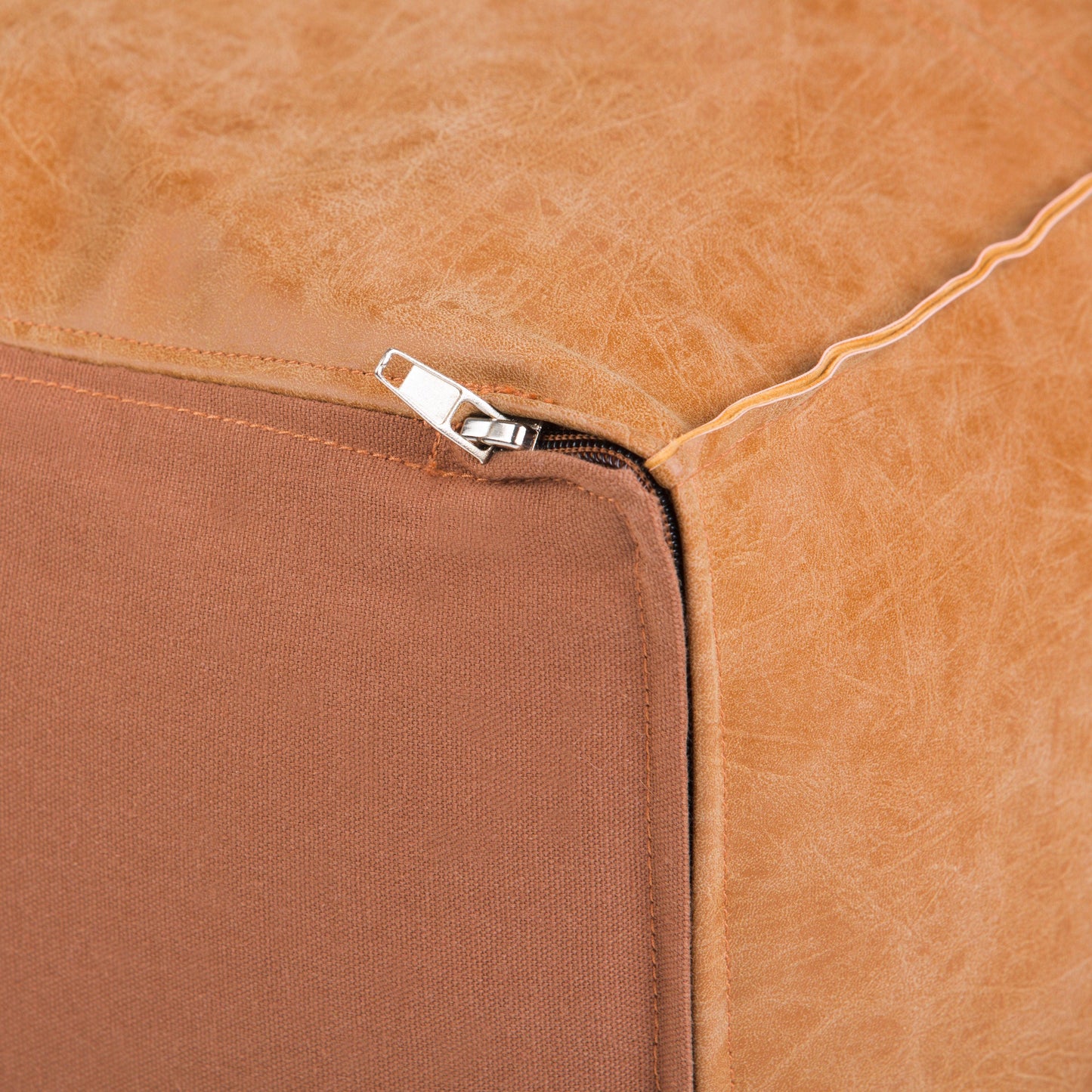 Close-up of the Brody - Versatile Square Pouf reveals a visible corner zipper where smooth brown leather on top meets a fabric-like material on the base.