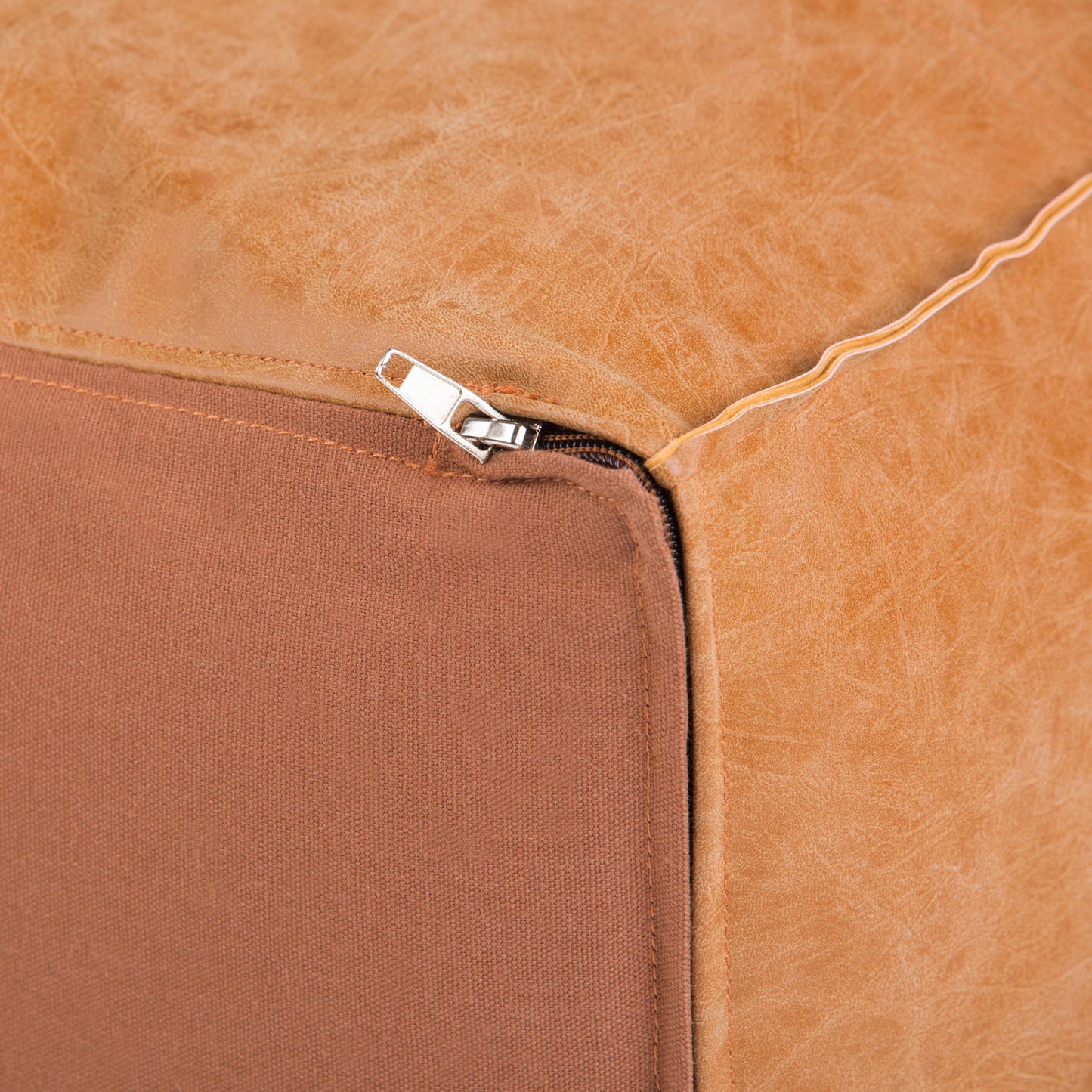 Close-up of the Brody - Large Square Coffee Table Pouf in tan leather, showing a partially opened silver zipper at one corner and the brown fabric underside.
