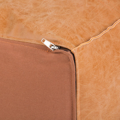 Close-up of the Brody - Large Square Coffee Table Pouf in tan leather, showing a partially opened silver zipper at one corner and the brown fabric underside.