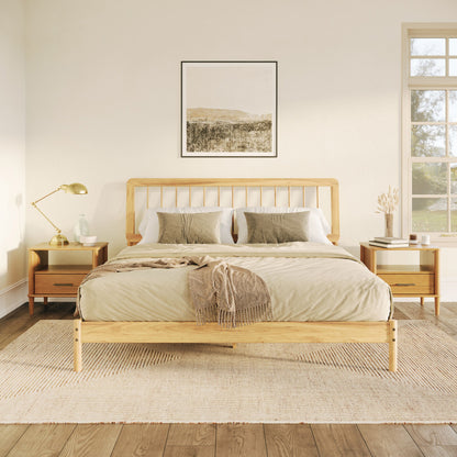 A cozy bedroom features the Mid-Century Modern Solid Wood Spindle Bed with beige bedding, green accent pillows, a brown throw, matching nightstands and lamps, a neutral rug, a large window, and landscape artwork above the bed.