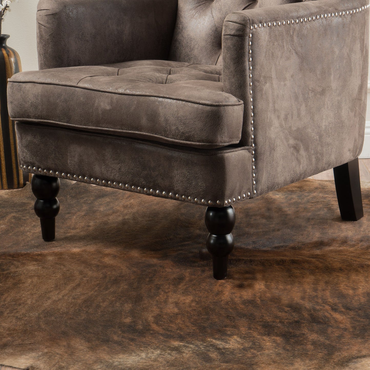 Close-up of the Vitality Club Chair featuring brown upholstery, button-tufted diamond stitching, nailhead trim, and turned wooden legs, set atop a brown cowhide rug.