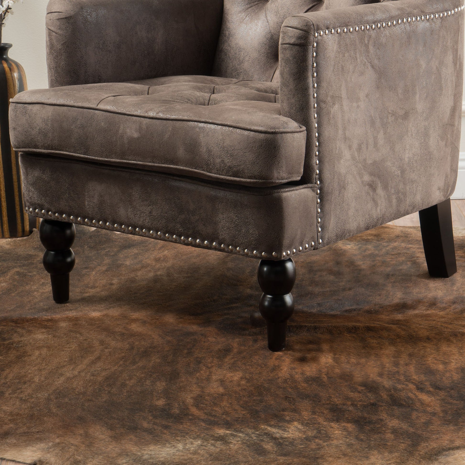 Close-up of the Vitality Club Chair featuring brown upholstery, button-tufted diamond stitching, nailhead trim, and turned wooden legs, set atop a brown cowhide rug.