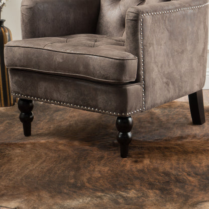 Close-up of the Vitality Club Chair featuring brown upholstery, button-tufted diamond stitching, nailhead trim, and turned wooden legs, set atop a brown cowhide rug.