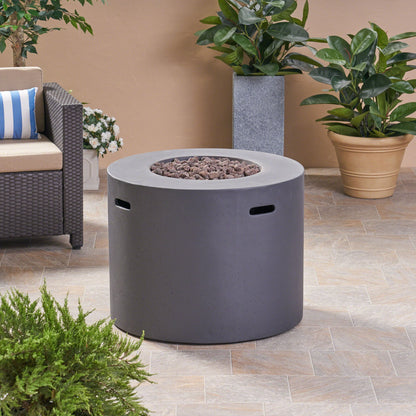 A Round Iron Fire Pit With 40,000 Btu and lava rocks sits on a tiled patio, surrounded by green potted plants and a wicker sofa with striped cushions.