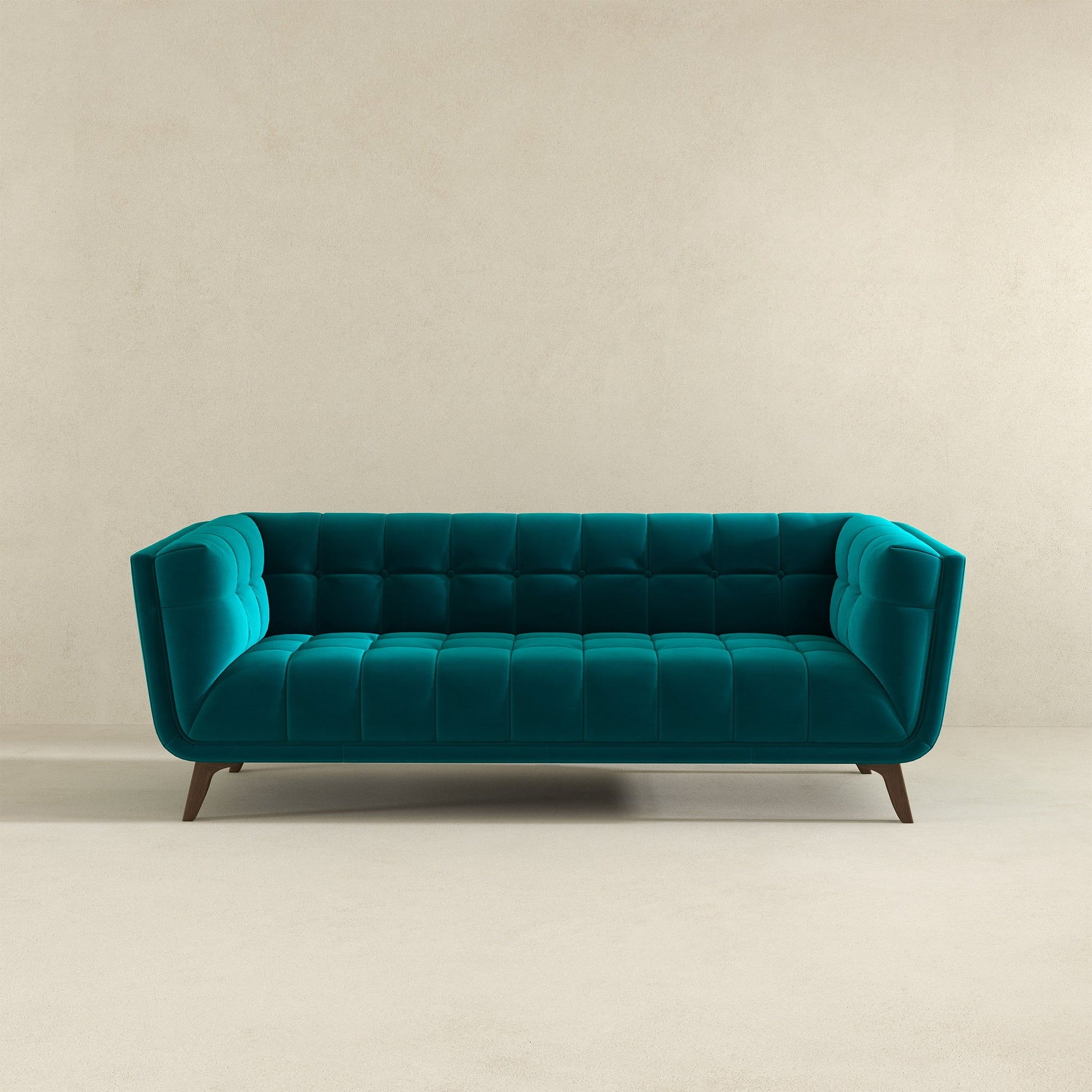 The Addison Mid-Century Modern Design Tufted Sofa, in teal velvet with tufted cushions and angled wooden legs, is set against a plain beige wall and a light floor.