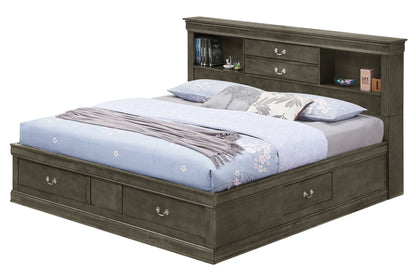 The Louis Phillipe Bookcase Storage Bed features storage drawers in the base and headboard, topped with a light blue floral comforter, gray blanket, and pillows. The headboard displays books, a clock, and small decor pieces.