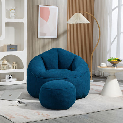 A cozy living room features the Bedding Bean Bag Sofa Chair High Pressure Foam with Footrest on a light rug, next to a round table, floor lamp, abstract wall art, and decor shelves. Sunlight pours through a large window.
