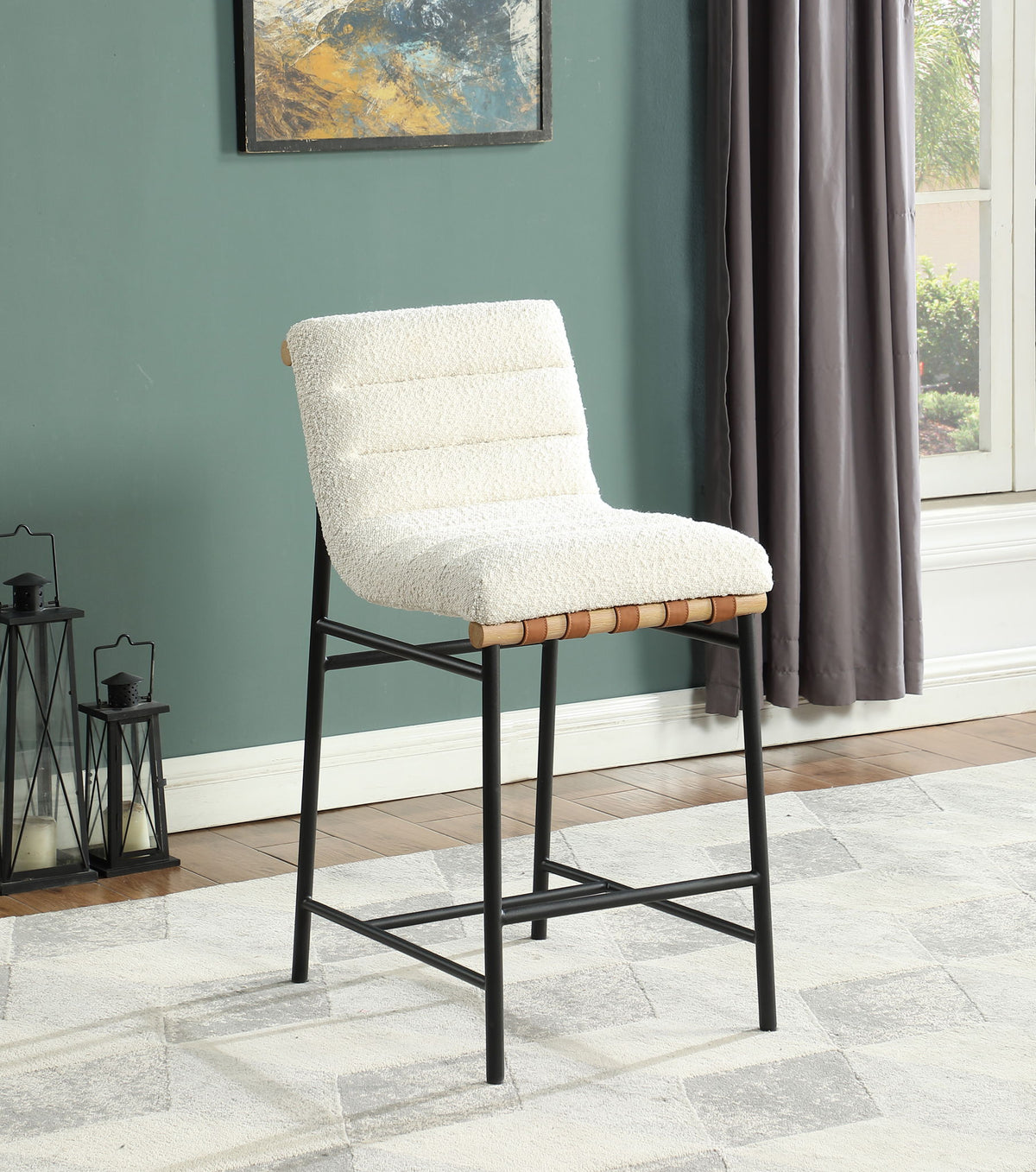 The Lahni 17" Boucle Fabric Counter Height Chair features a modern white upholstered seat, black metal legs, and textured cushion, shown on a patterned rug in a green-walled room with a window and decorative lanterns.